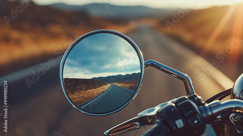 A close-up of a motorbike’s rearview mirror, reflecting the open road behind, with the mirror and handlebars occupying most of the frame.