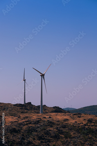  A row of wind turbines atop a rural hillside, captured against a clear evening sky. This image symbolizes renewable energy and sustainability, highlighting the beauty of eco-friendly power generation