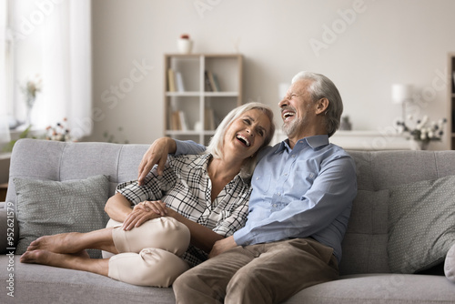 Joyful mature wife and husband resting together on couch, hugging, talking and laughing enjoy time together, joking, having fun, relish their harmonic relations, understanding and joint sense humour