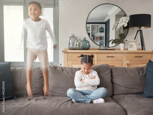 Frustrated little girl, sofa and jumping with sibling in chaos, hyperactive or dispute in living room at home. Female person, children or kids in unfair playtime, energetic or mixed emotions at house