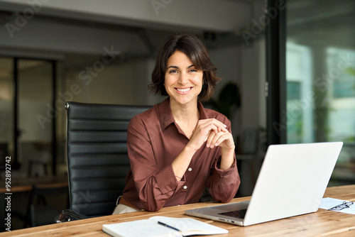 Smiling Hispanic young woman entrepreneur, happy female executive manager looking at camera sitting at workplace with laptop. Portrait of confident businesswoman leader in her 30s at work desk.