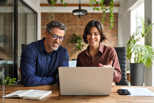 Two busy happy professional business man and woman executive leaders team using laptop working on computer at work desk having conversation on financial project at meeting in office.