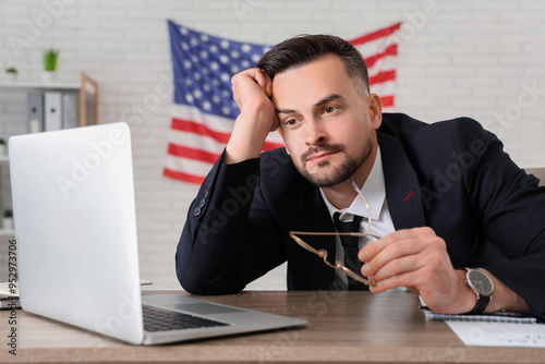 Handsome young tired businessman with flag of USA in office