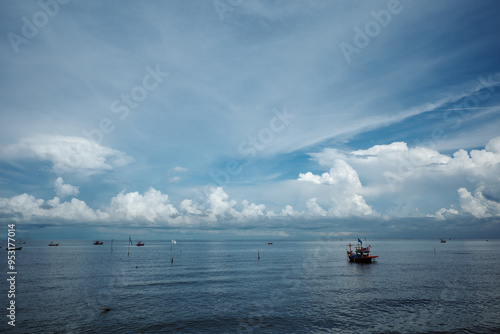 A serene coastal scene featuring a wide expanse of calm sea with scattered fishing boats gently floating on the water in Chon buri, Thailand.