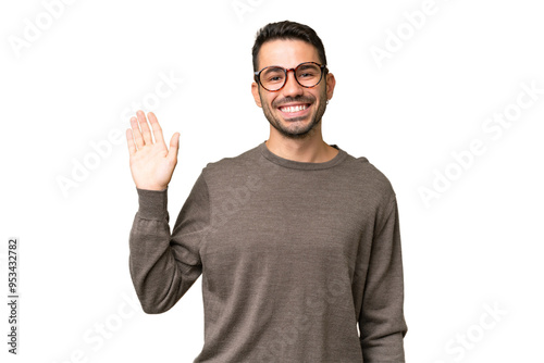 Young handsome caucasian man over isolated background saluting with hand with happy expression