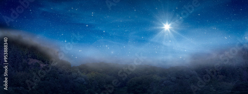 Bright star indicates the Nativity of Jesus Christ in the starry sky and fog rises in the mountains above the night forest.