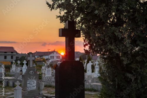 Bloody sunset in a cemetery with a black marble cross outlined in the foreground