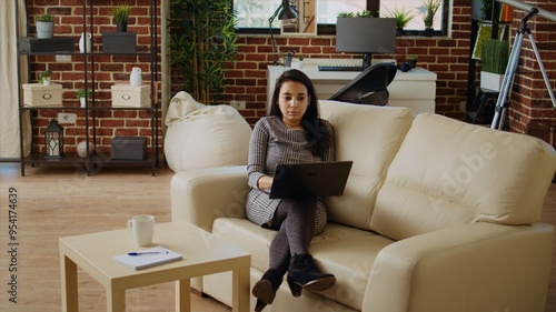 Self employed woman focused on finishing dull monotonous job tasks while staying at home in nice apartment. Freelancing businesswoman typing on laptop keyboard, lounged on couch, camera A panning shot