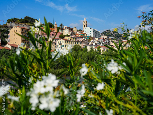 **Title:** Charming Coastal Town Of Ventimiglia In Southern Europe With Colorful Houses, Lush Greenery, Vibrant Flowers, Serene River, And Clear Blue Sky Under The Warm Sun In Italy's Picturesque Land