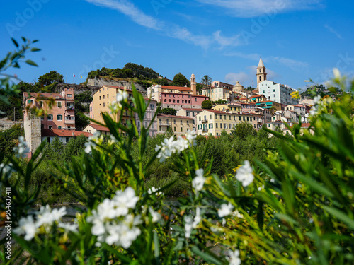 **Title:** Charming Coastal Town Of Ventimiglia In Southern Europe With Colorful Houses, Lush Greenery, Vibrant Flowers, Serene River, And Clear Blue Sky Under The Warm Sun In Italy's Picturesque Land