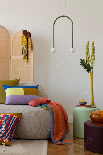 Contemporary interior design featuring a curved sofa, vibrant throw blankets, and geometric pillows, accented by a minimalist hanging lamp.