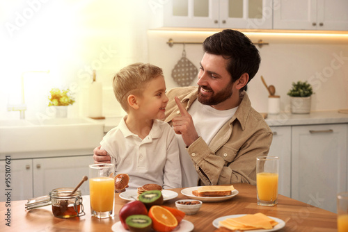 Father and his cute little son having breakfast at table in kitchen on sunny morning