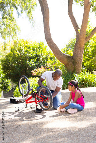 Fixing bicycle, father and daughter bonding outdoors in sunny park