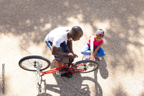 Fixing bicycle, father teaching daughter how to repair bike outdoors