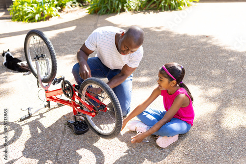 Repairing bicycle in driveway, father and daughter bonding outdoors