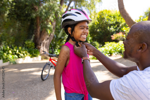 Father helping daughter with bicycle helmet, preparing for outdoor activity