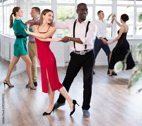 With unhurried music, woman with African man in couple spins to rhythm of waltz during lesson for novice students. Classes in mini-groups for those who want to learn dancing