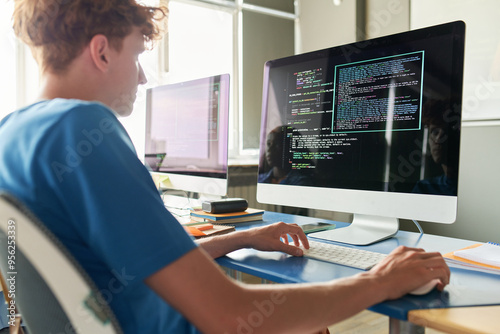 Side view of student sitting at desk with computer and typing programming code during IT class in school or college