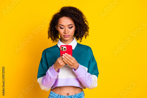 Photo of focused woman with curly hairstyle dressed striped top look at smartphone in hands chatting isolated on yellow color background