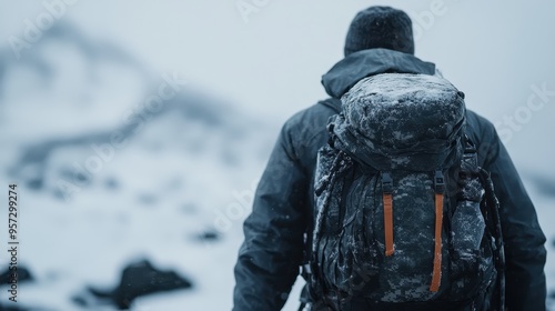 A person fully equipped with winter gear including a large backpack and warm clothing is seen from behind as they hike up a snow-covered mountain, epitomizing solitude and determination.