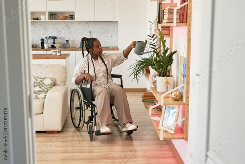 Person in wheelchair watering plants on shelf in cozy, modern apartment with wooden flooring and white furniture, creating an inclusive, homey environment