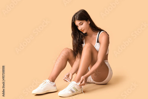 Sporty young woman tying shoelaces on beige background