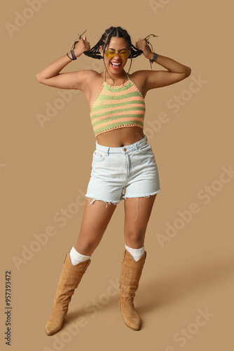 Emotional young African-American woman in sunglasses with dreadlocks on brown background