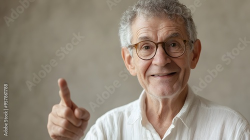 An elderly man with glasses, short curly hair, wearing a white shirt, pointing with a gentle smile, soft-focus neutral background