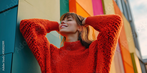 Joyful woman in vibrant orange sweater smiling against colorful wall background