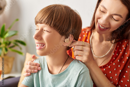 A mother lovingly assists her son with his hearing aid while smiling together.