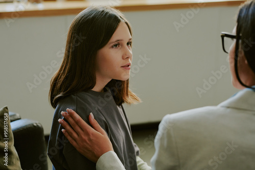 Young girl with long brown hair engaged in conversation with an adult hand on shoulder providing comfort and warmth atmosphere