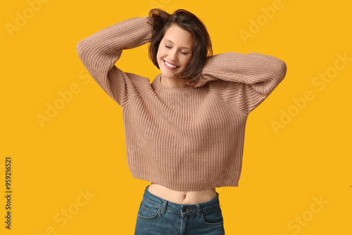 Happy young woman in stylish brown sweater on yellow background