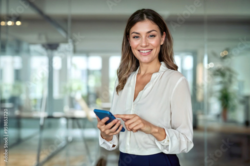 Happy mature professional business woman using cell phone at office, portrait. Smiling mid age 45 years old businesswoman executive standing at work lobby holding smartphone looking at camera.