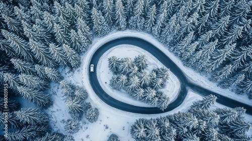 An aerial perspective displays a curving road navigating through a snowy forest