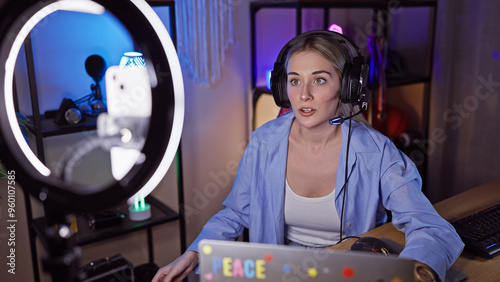 A focused young woman with blonde hair engages in streaming in a modern gaming room at night.