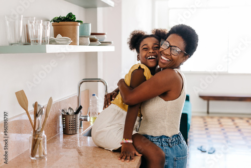 Mama's love: Happy black mom hugging her daughter in the kitchen