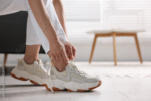 Woman tying shoelace of sneaker indoors, closeup. Space for text