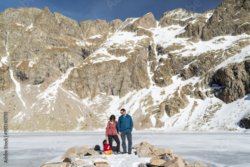 Family with one child at a frozen pyrenean lakeshore called Ibón del Sen in Chistau Valley.