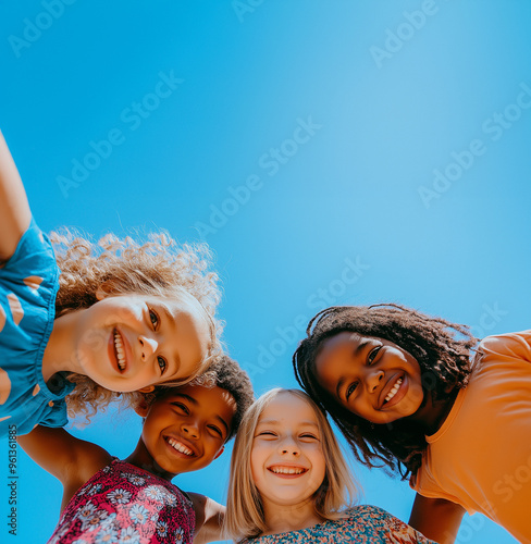 A photo of diverse, happy children looking down at the camera, smiling and posing for an advertising campaign in front of a blue sky. Group portrait of happy kids huddling. Friendship concept.