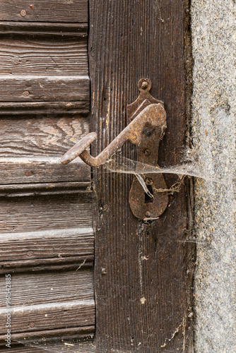 Old brown wooden door in Austria Europe with a rusty door handle and a keyhole with cobwebs that hasn't been opened for a long time.