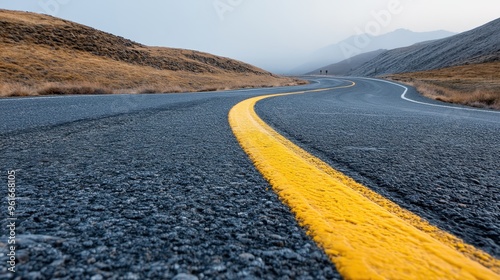 A wide-angle perspective of a winding road with a yellow centerline, cutting through dry, barren hills, representing an ongoing journey through a desolate yet picturesque landscape.