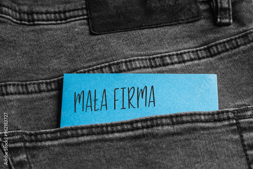 Blue card with a handwritten inscription "Mała Firma", inserted into the pocket of gray pants jeasnow (selective focus), translation: Small Business