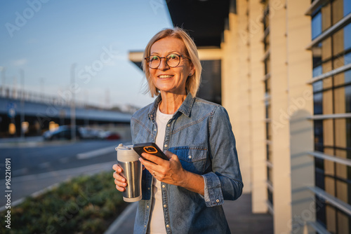 Mature woman wait for the bus and hold mobile phone and thermos