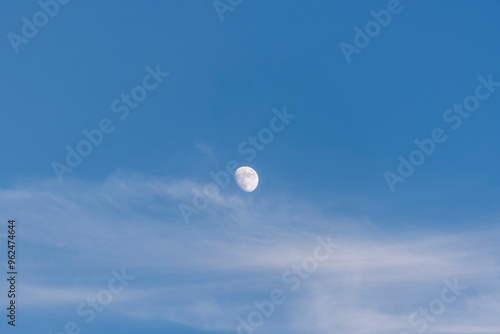 A serene moon captured in a blue daytime sky with soft clouds, conveying calm and peace.