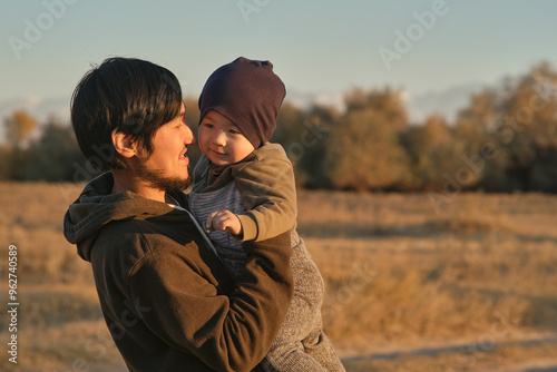 Father holding baby boy in autumn field at sunset.