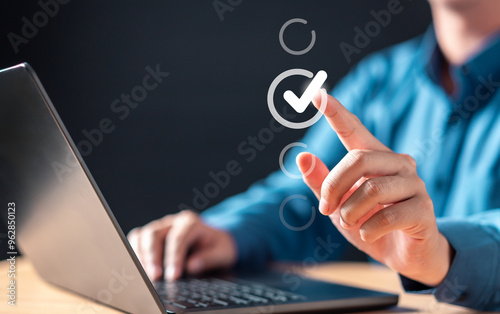 quality, confirmation, check, validation, approval, checkbox, voting, status, tick, touch. A man is using a laptop and pressing a button that a check mark on it. Concept of accomplishment.