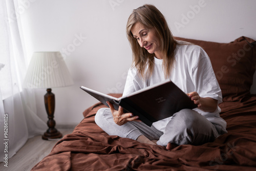 Middle aged woman looking at photo album while sitting on bed