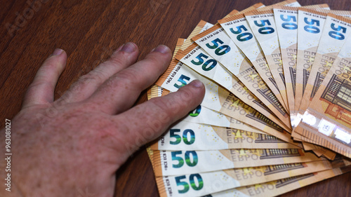 Male's Hand Holding EURO Banknotes on Brown Wooden Table. paper money, currency, cash, close-up. concepts of finance, payments, commerce, financial transactions, prosperity. 50 euro denomination