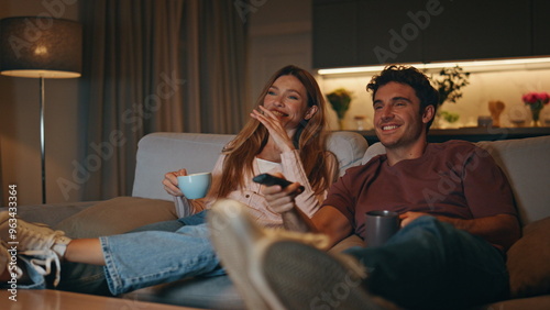 Married couple resting couch together. Smiling husband switching tv channels