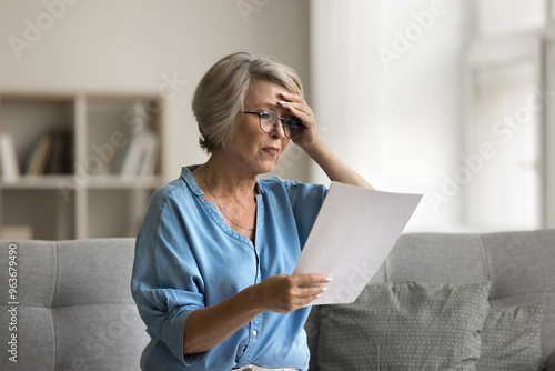 Older woman reading document that made her frustrated, receive bad, upsetting news related to financial troubles, health concerns, eviction or bank debt notification, unexpected bills, feel distressed